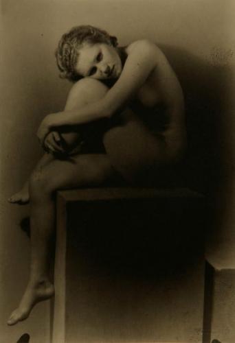 A nude female sitting on cube